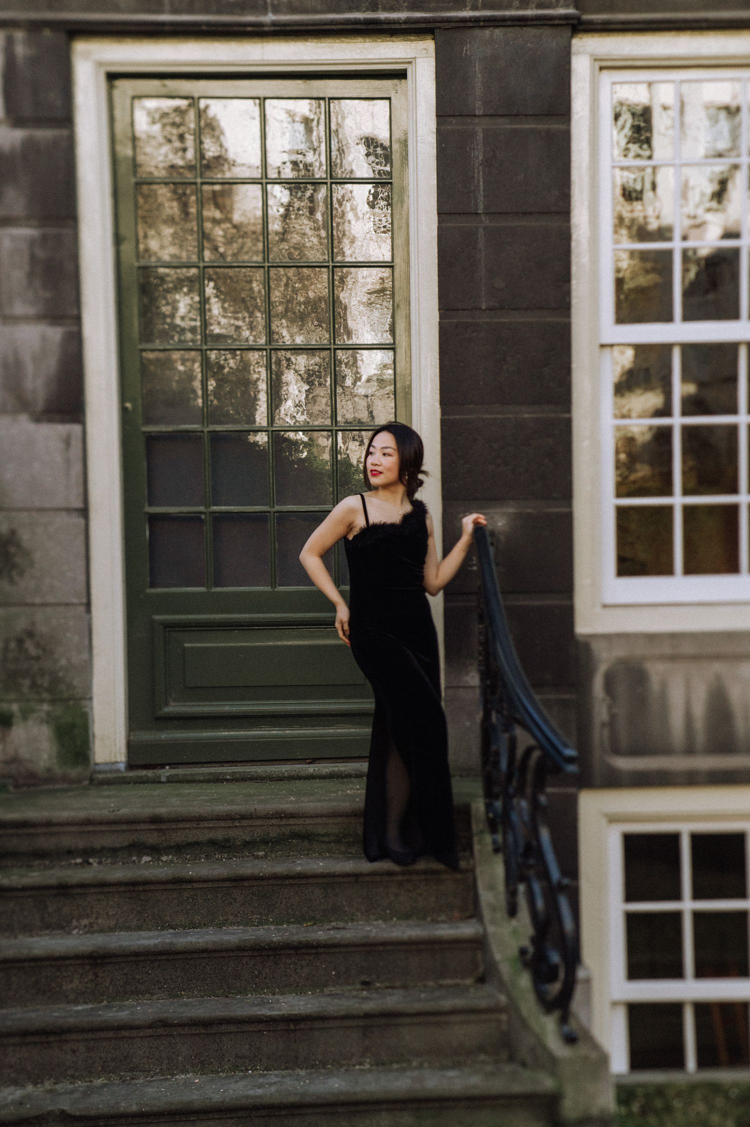 A woman in a black evening gown poses on stone steps in front of a historic building.
