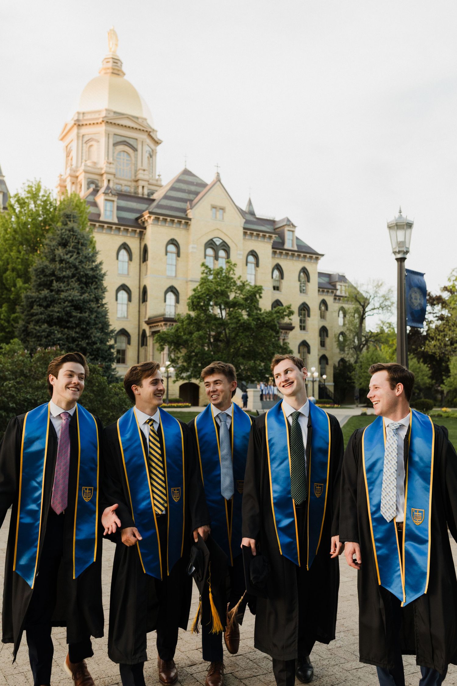 Graduates in blue stoles and black robes standing by Notre Dame's golden dome building.