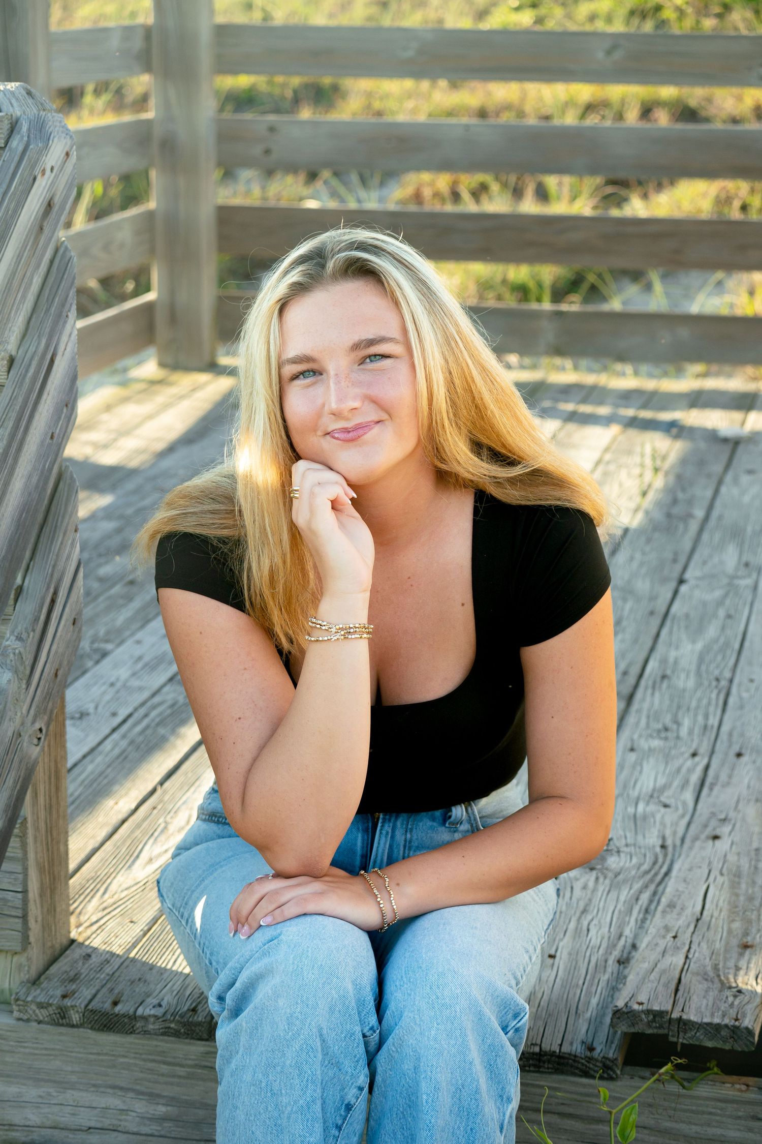 Casual portrait of woman in black shirt and jeans sitting on wooden boardwalk.