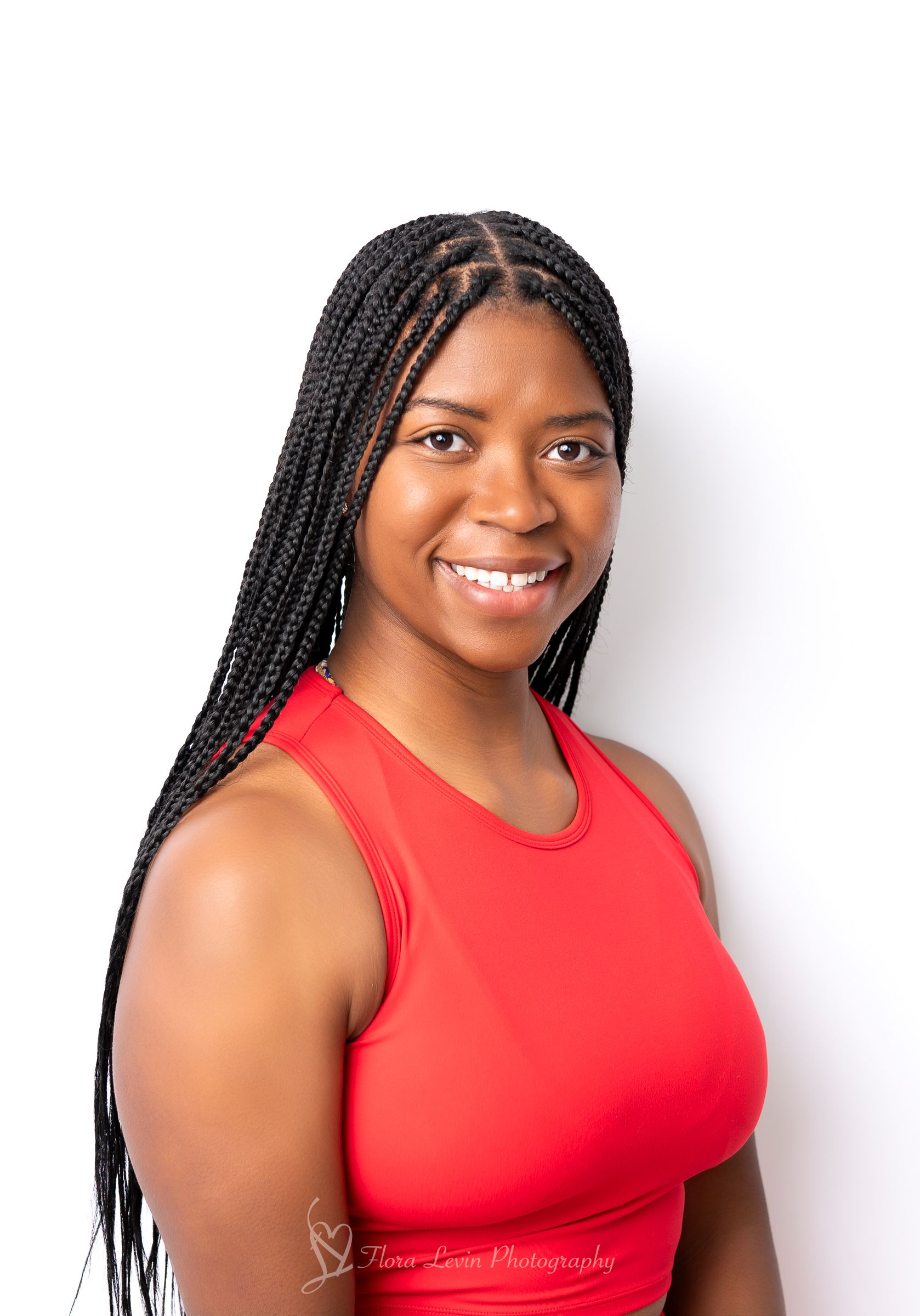 A young  woman headshot with long braids smiles confidently in a red tank top against a white background.