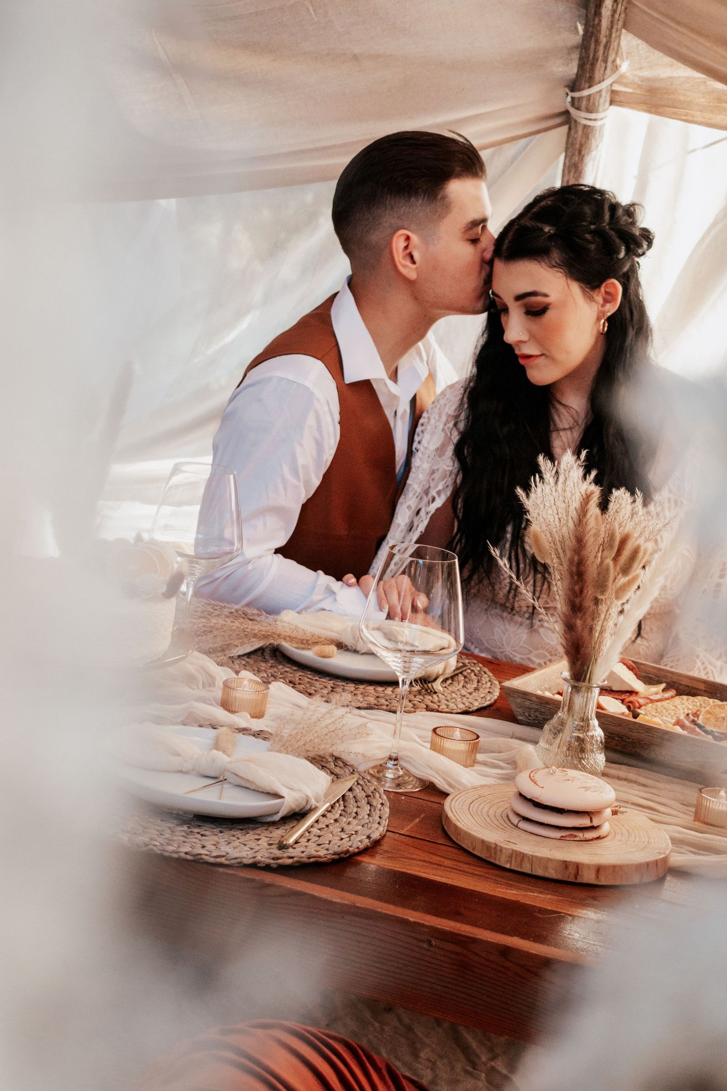 A cozy indoor engagement session featuring a couple sharing a rustic picnic setup with dried florals and warm earth-toned details in a boho-