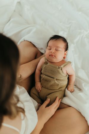 A sleeping baby in brown overalls rests peacefully on white bedding.