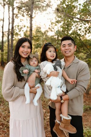 A family in coordinated neutral outfits poses together in an autumn forest setting.
