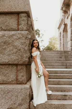A bride in a white dress sits gracefully on stone steps during a wedding photoshoot.