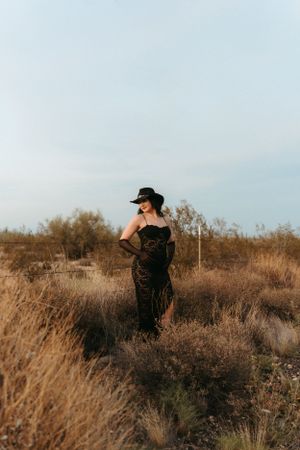 A photographer in black clothing takes photos in a field of tall grass at sunset.