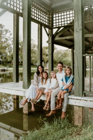 Family sitting together on wooden pier overlooking water during sunset photo session.