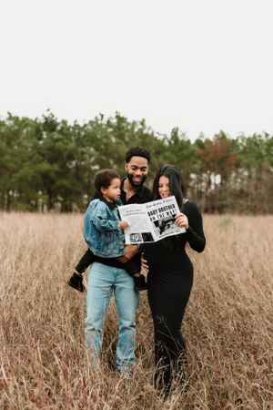 A couple shares a playful moment reading newspapers together in a tall grass field.