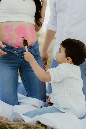Baby in white shirt reaches up while sitting on grass during outdoor photo session.
