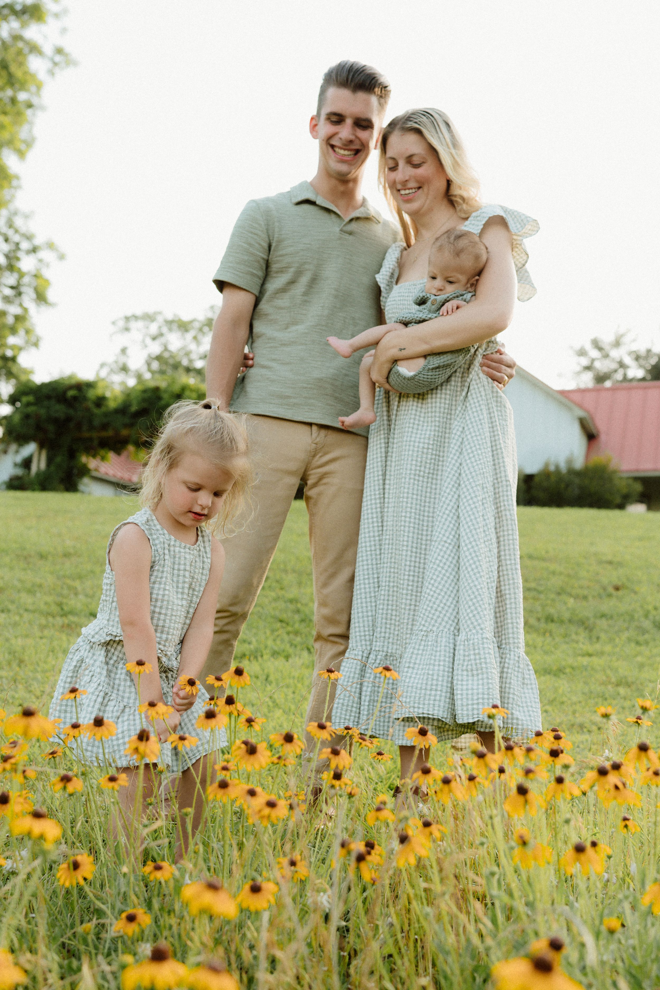 Family in coordinating outfits poses together in field of bright yellow wildflowers.