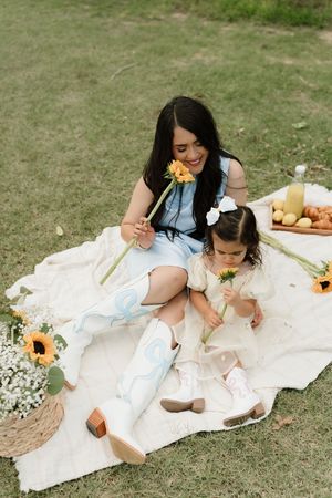 Picnic scene on white blanket with sunflowers and fresh food in grassy field.