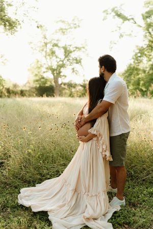 Romantic couple embraces in flowing dress during golden hour field photoshoot.