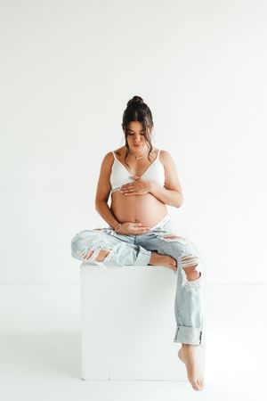 Woman in casual attire poses on white platform during minimalist studio session.