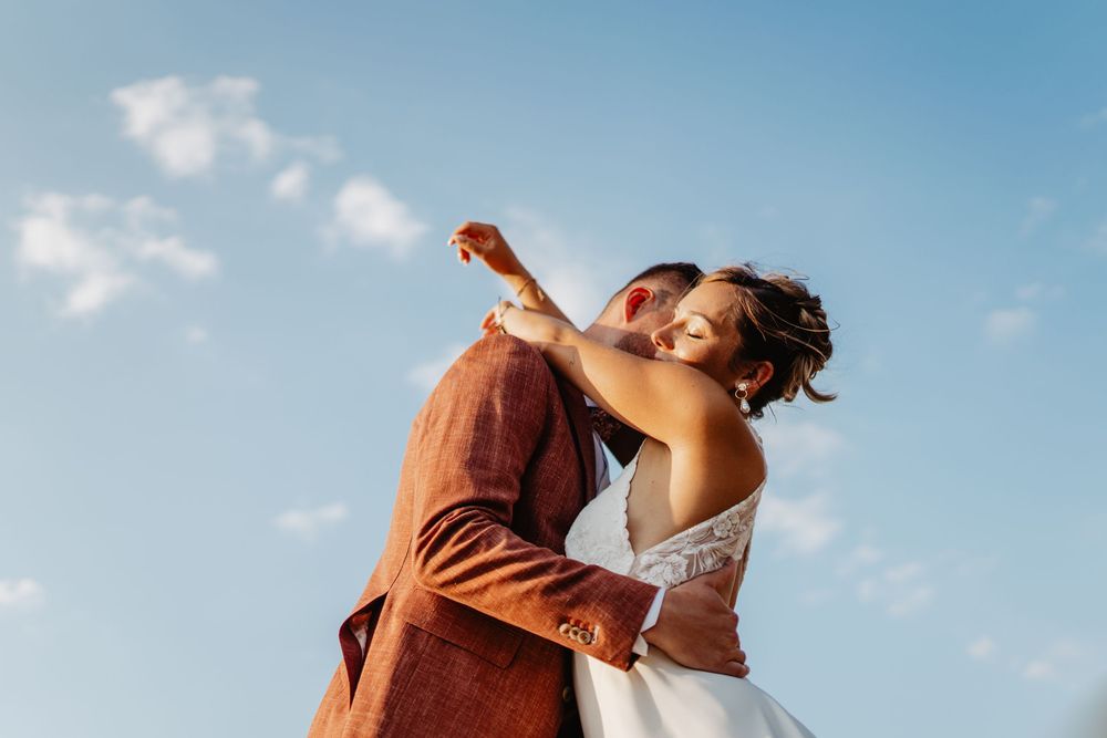 A joyful bride and groom embrace under a blue sky, celebrating their wedding day outdoors.