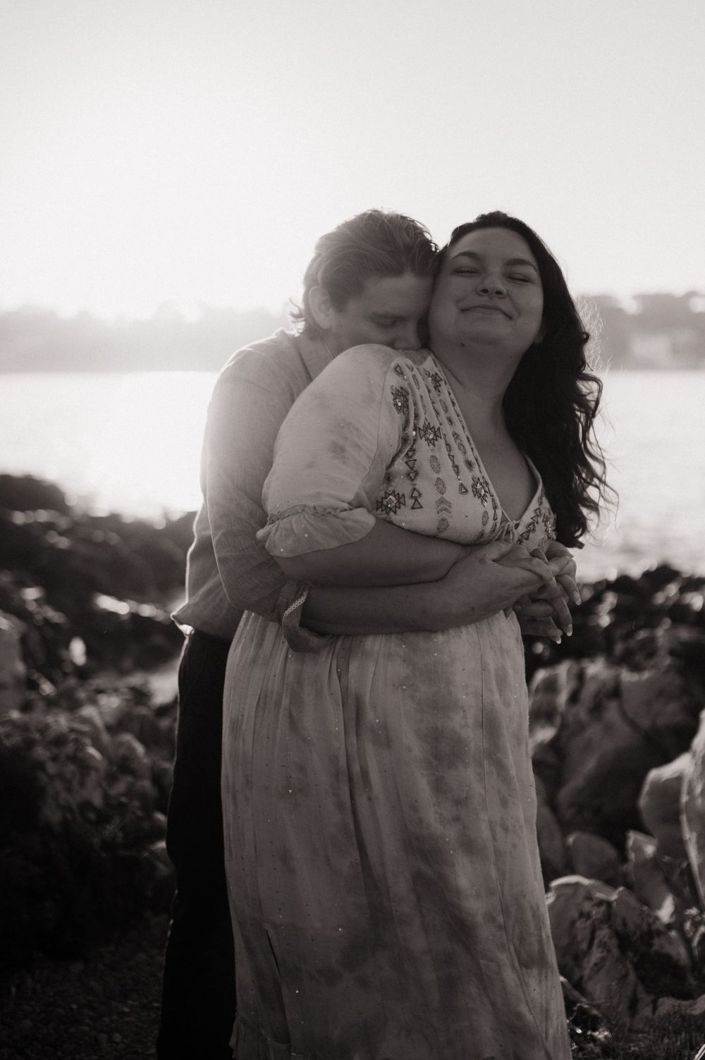 Photo en noir et blanc d'un couple s'enlacent chaleureusement au coucher du soleil