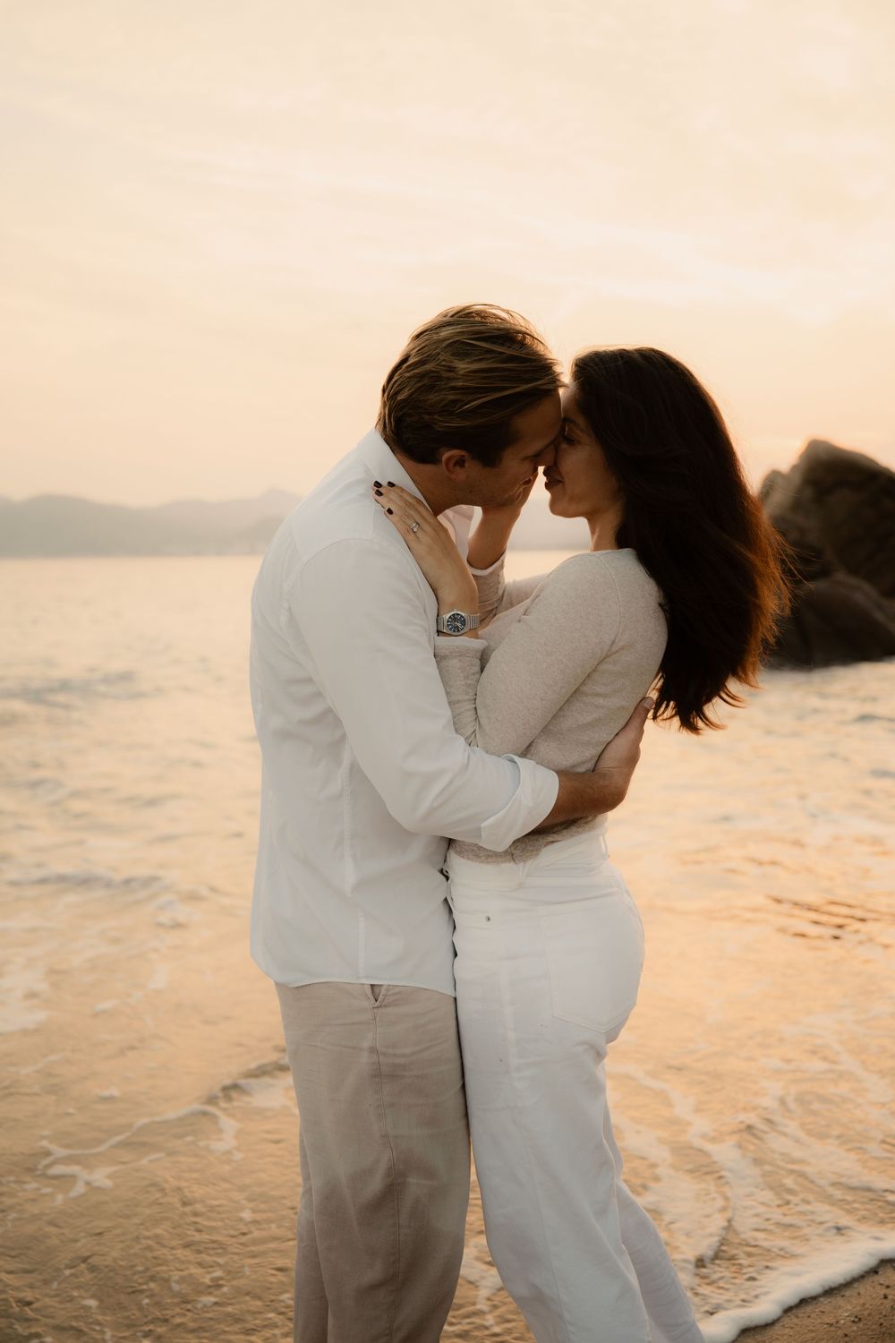 Deux amoureux s'enlacent tendrement au coucher du soleil en bord de mer.
