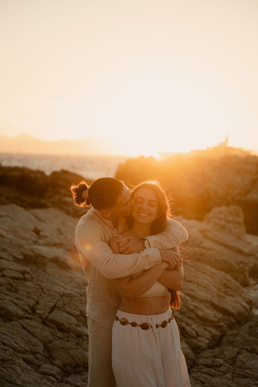 Un homme fait un câlin à une femme qui sourit de ce moment au coucher du soleil dans les roches blanchent de Juans les pins.