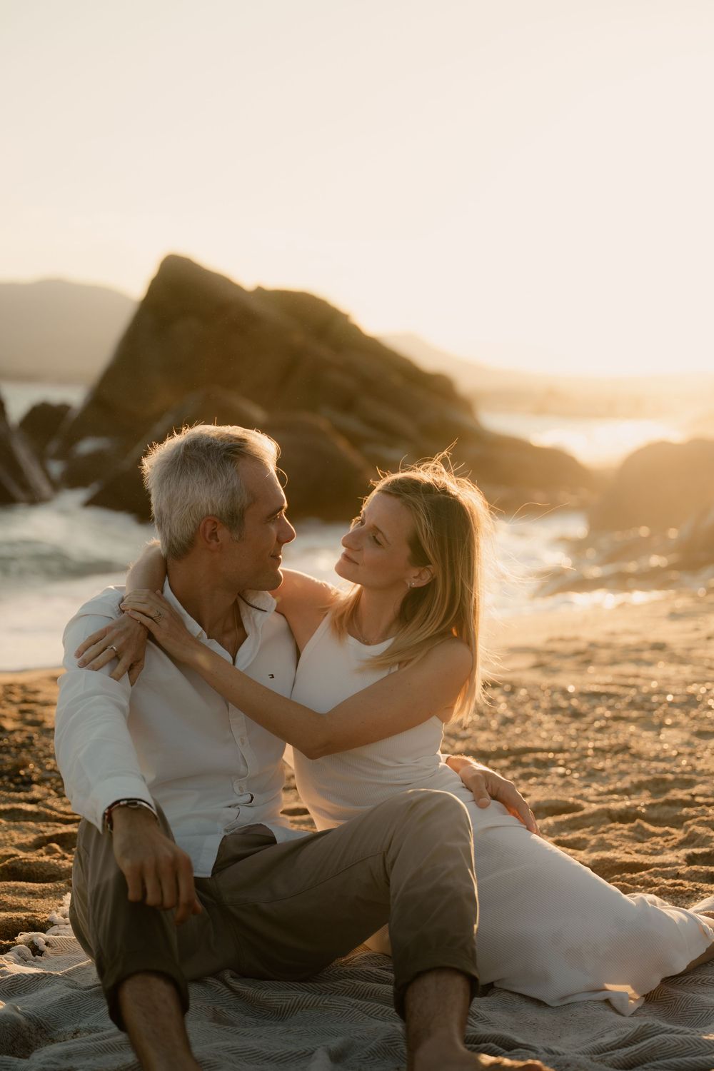 Un couple romantique assis ensemble sur une plage de sable au coucher du soleil, savourant des moments intimes dans une lumière dorée.