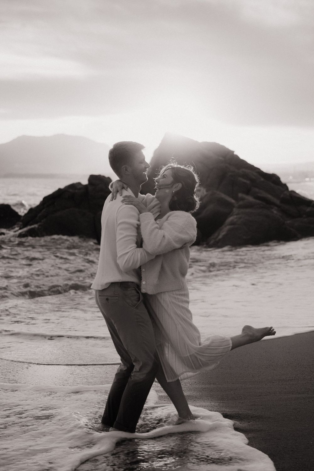 Une série de photos romantiques en noir et blanc montre un couple dansant et s'enlaçant sur une plage au coucher du soleil à Cannes.