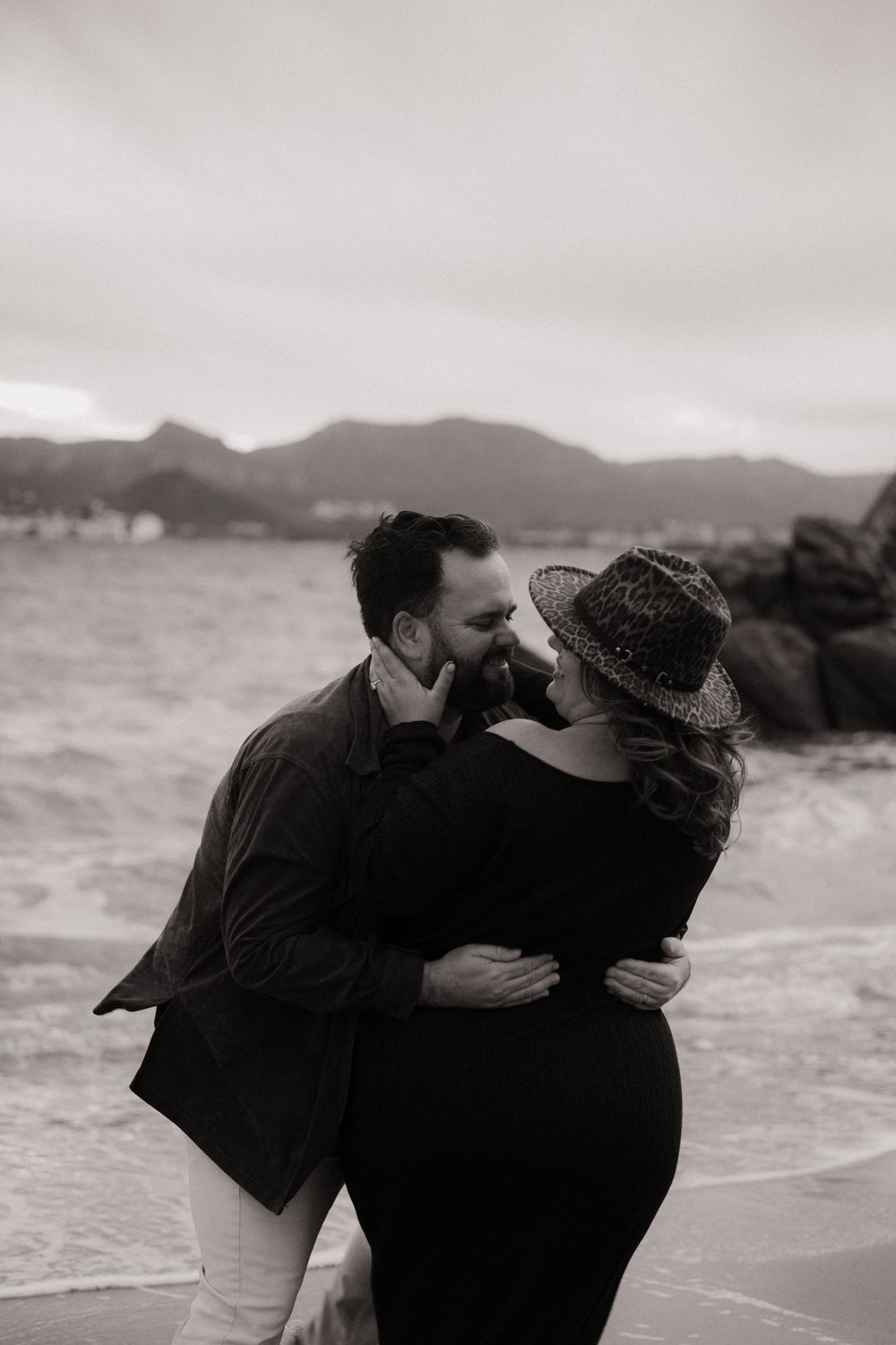Une série de photos romantiques en noir et blanc d'un couple enlacé sur une plage avec des collines en arrière-plan.