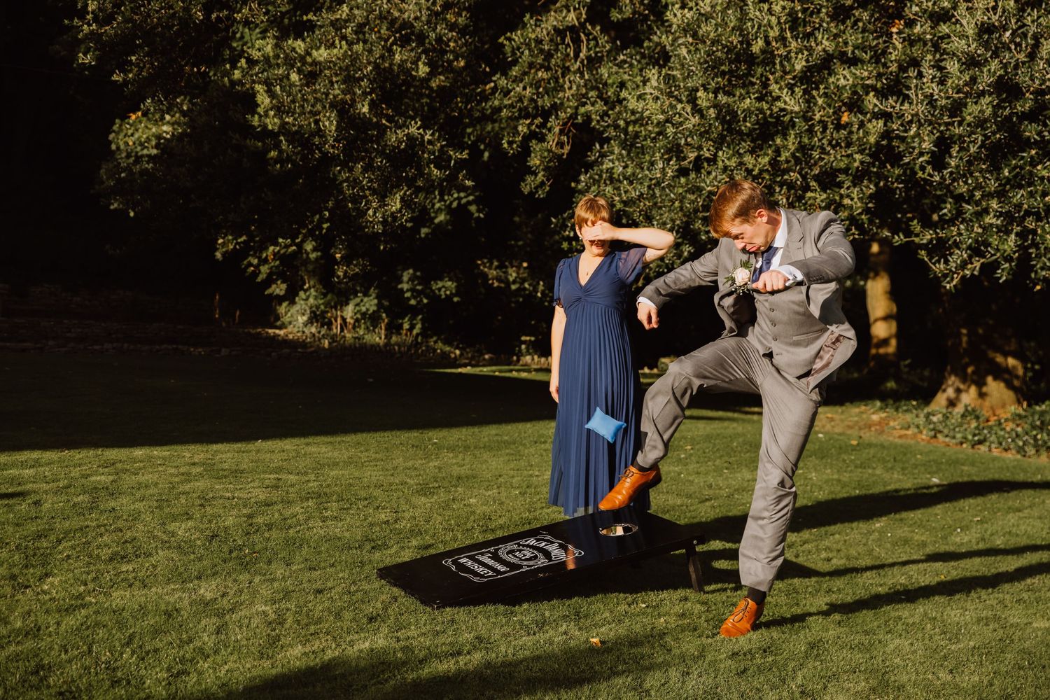 Bridesmaid and Groomsmen playing garden games at Upwey House. Groomsmen is kicking a bean bag. Wedding games Dorset. Dorset Wedding venue