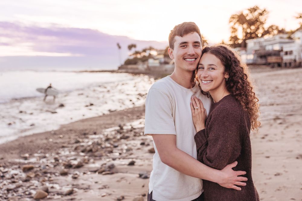 A couple embracing on a coastal beach during golden hour sunset.
