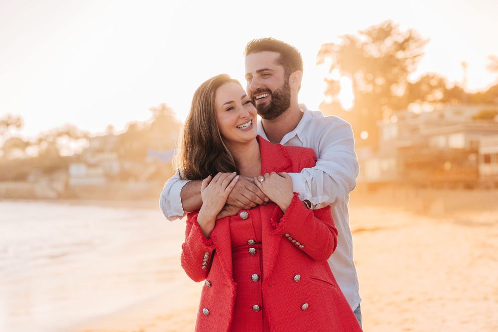 A romantic embrace during golden hour sunset with a woman wearing a bright red coat.