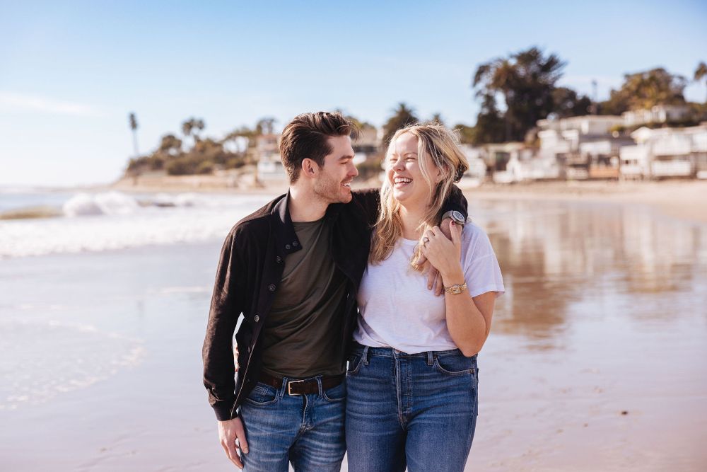 A happy couple shares a joyful moment while walking together on a scenic beach.