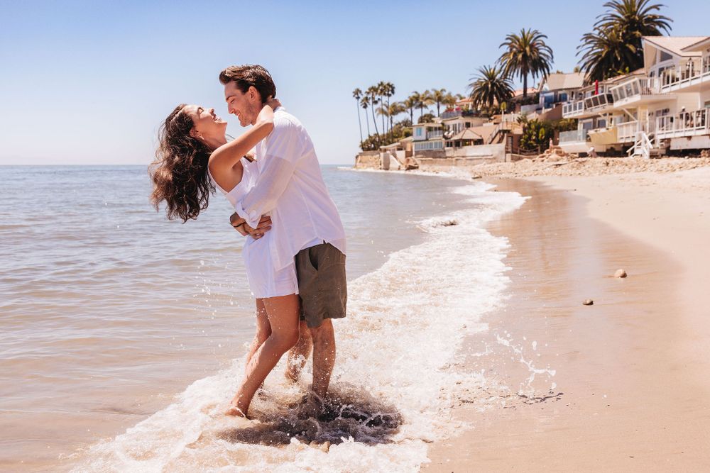 A happy couple embracing and celebrating on a beautiful California beach with palm trees.