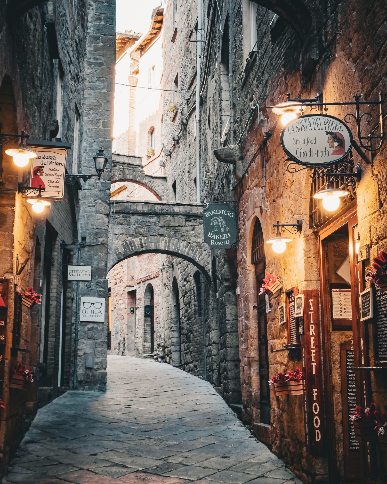 A charming medieval stone alleyway with arches and glowing lanterns in an Italian town.