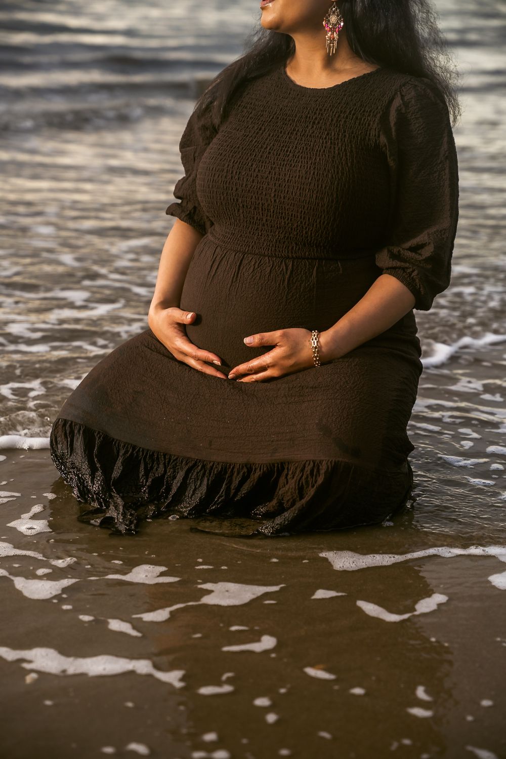 Close-up of black dress with fringe detail in ocean waves during beach maternity shoot.