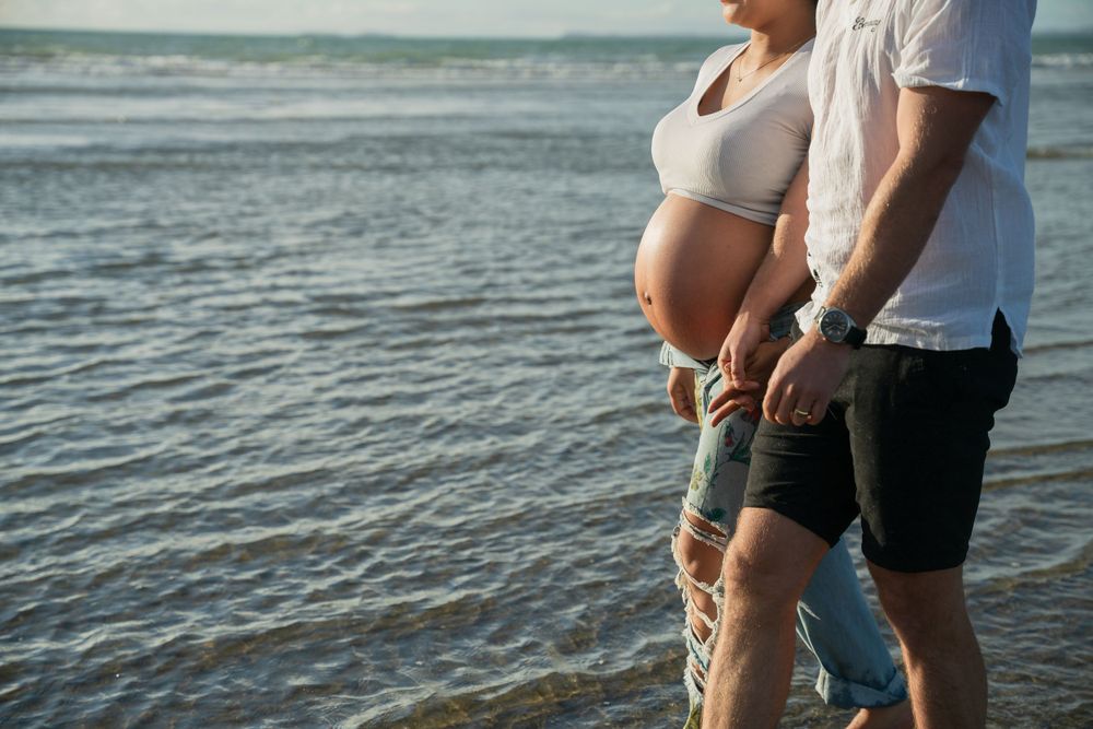 Side view of expectant couple standing together by the ocean.