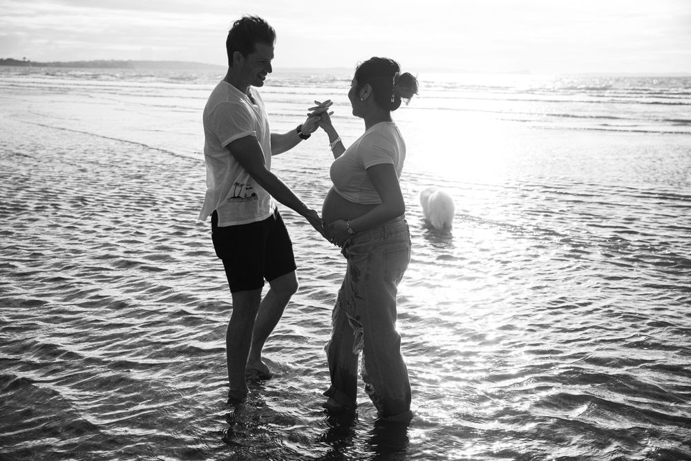 Black and white photo of couple sharing intimate moment on beach at sunset.