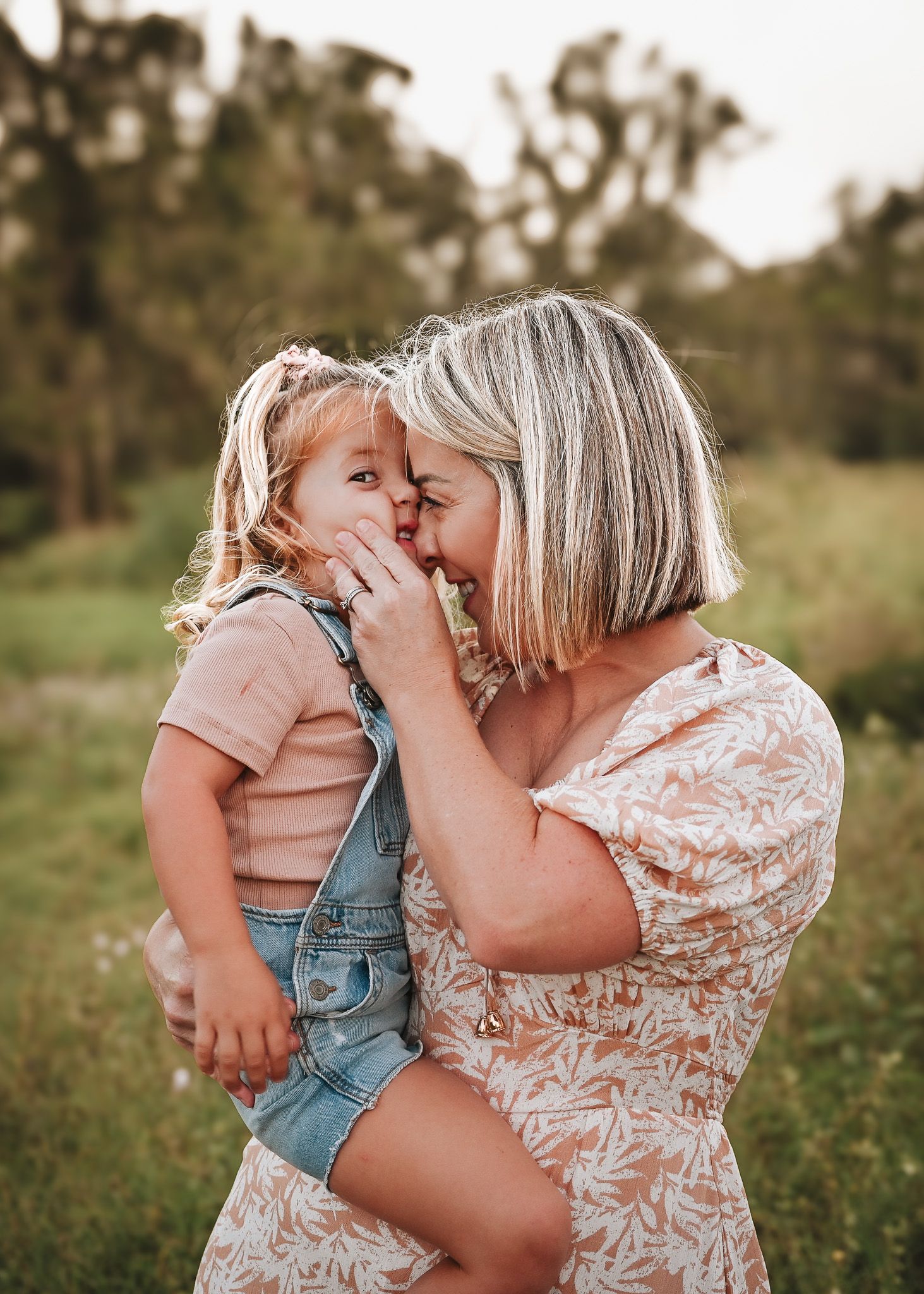 Mother and toddler share intimate moment outdoors in summer clothing.