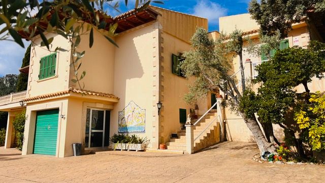 Mediterranean villa with cream walls, green shutters, and exterior staircase in a garden setting.