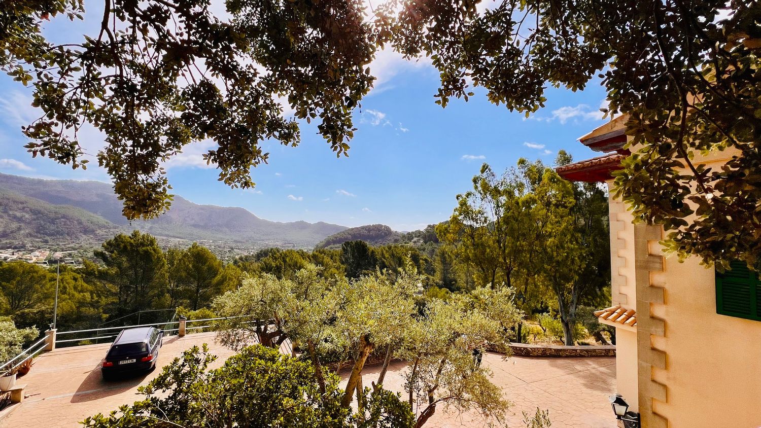Mountain vista framed by overhanging tree branches with Spanish-style architecture in foreground.