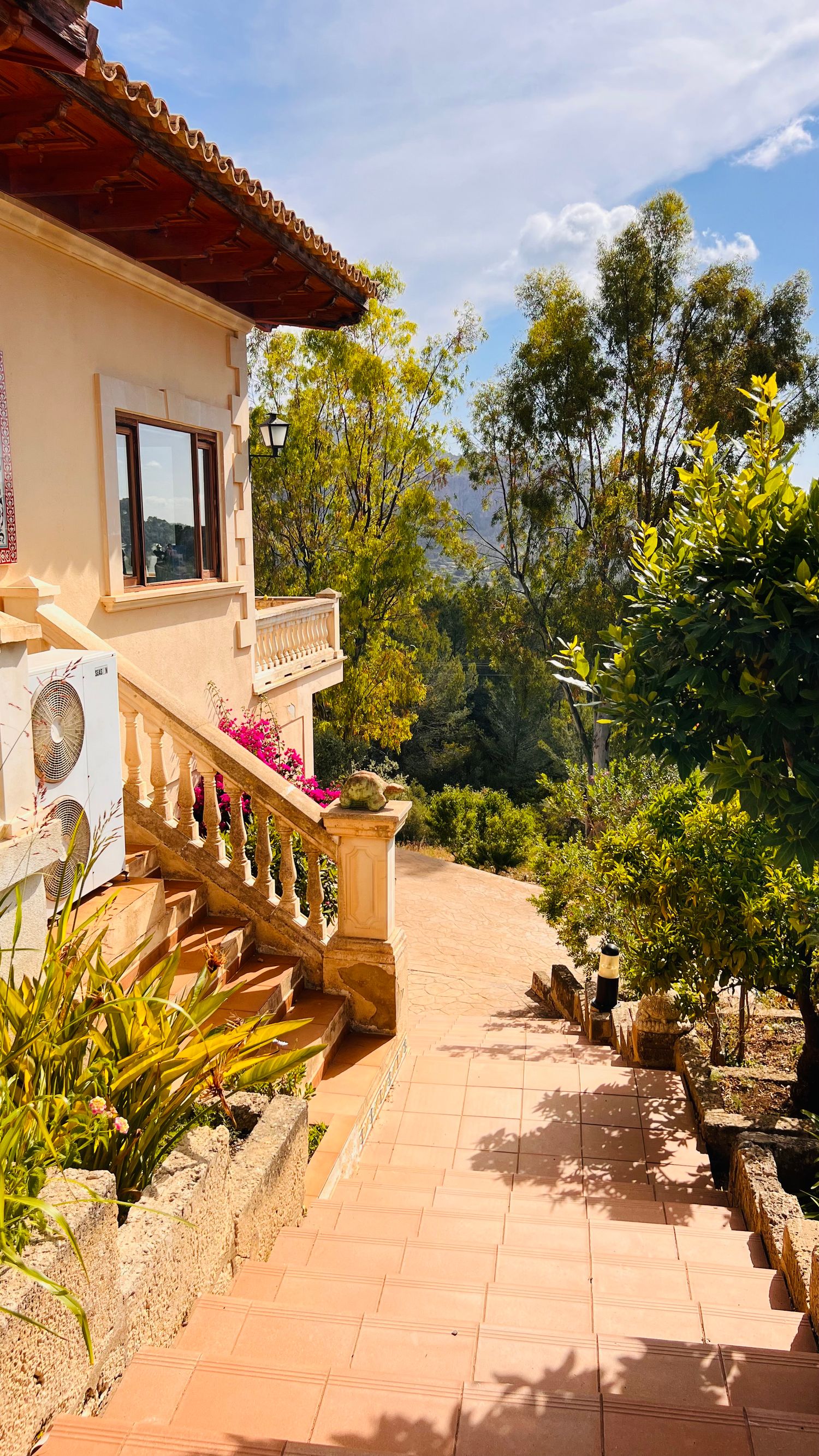 Mediterranean villa balcony with terracotta tiles and ornate stone balustrade overlooking lush mountain landscape.