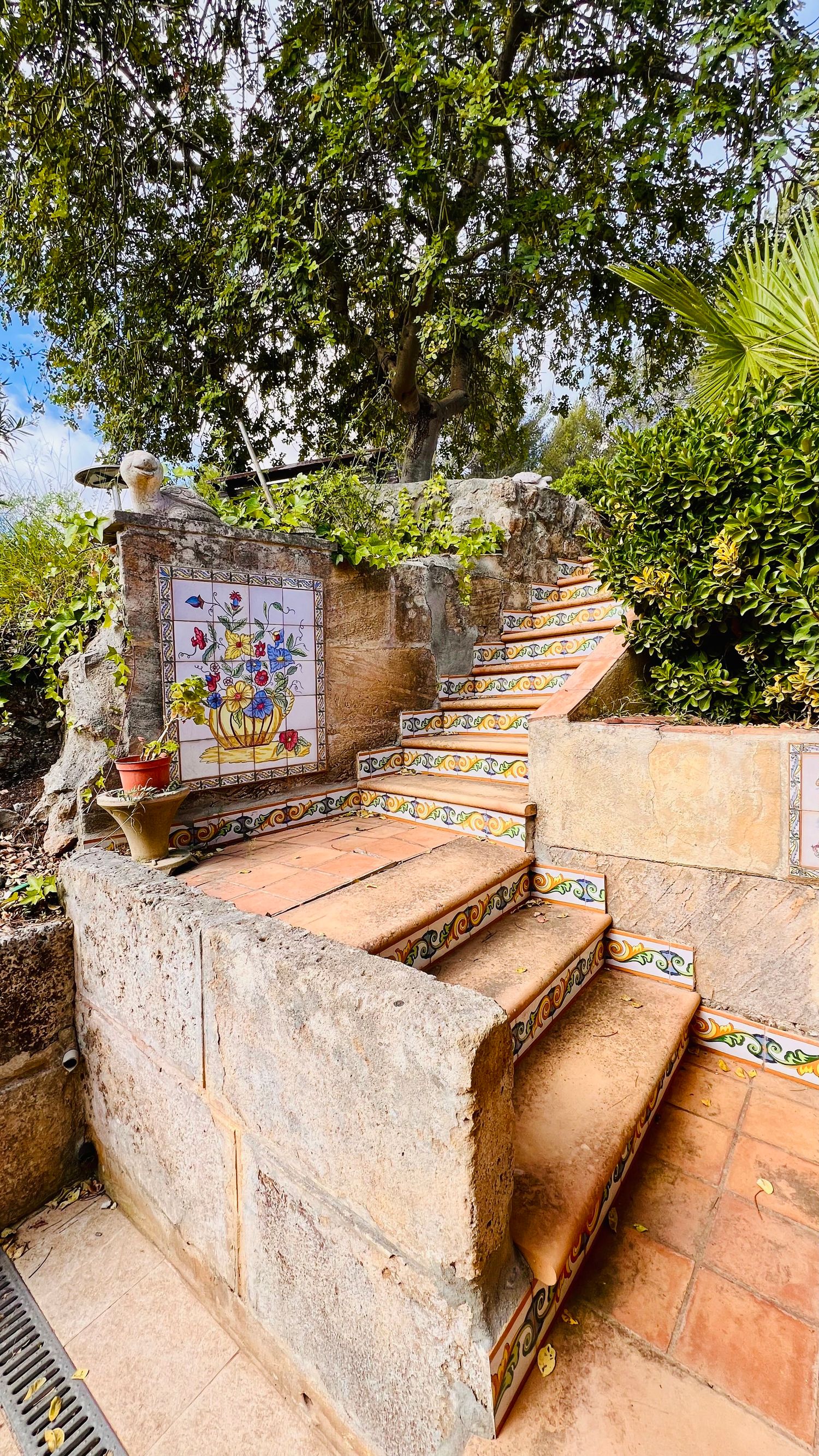 Decorative tiled steps with colorful ceramic details lead upward through a Mediterranean garden.
