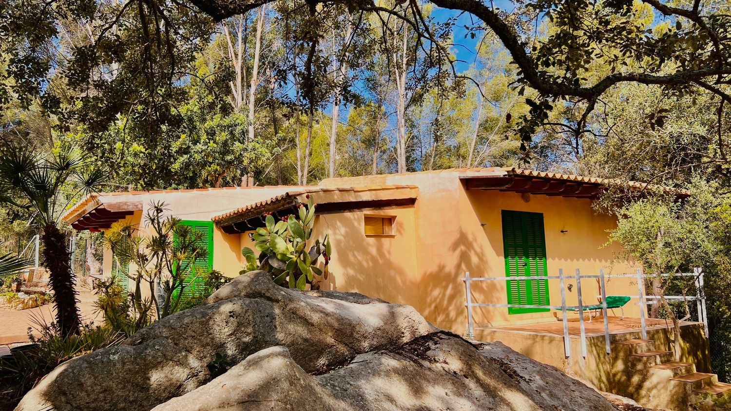 A rustic adobe cottage nestled among large boulders and trees in a natural setting.