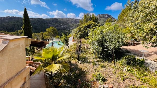 Hillside Mediterranean property with cypress trees and lush landscaping against mountain backdrop.