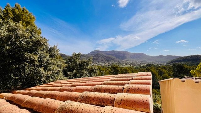 Scenic mountain landscape view over terracotta roof tiles against a bright blue sky.
