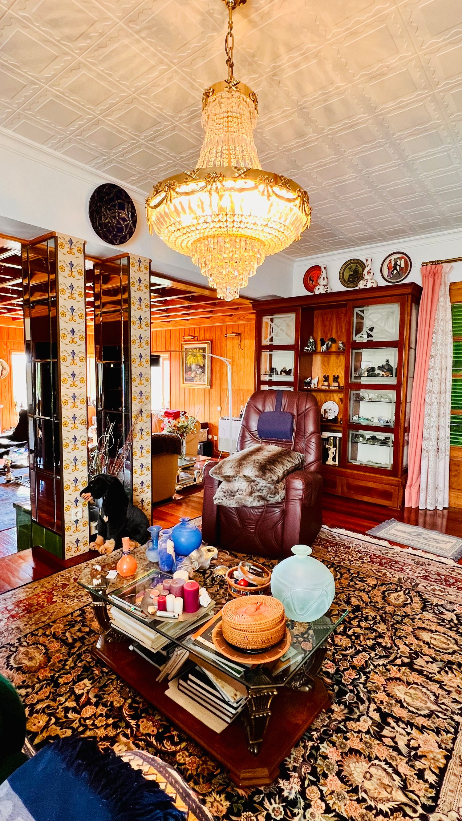 Elegant living room with crystal chandelier, leather chair, and ornate decor on a patterned rug.