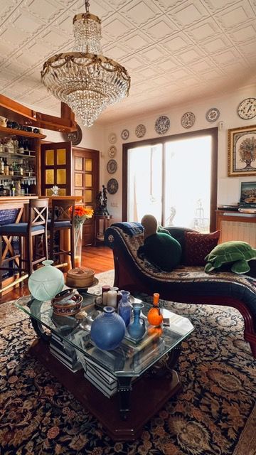 Opulent living room featuring crystal chandelier, ornate bar, and vintage chaise lounge with decorative plates.