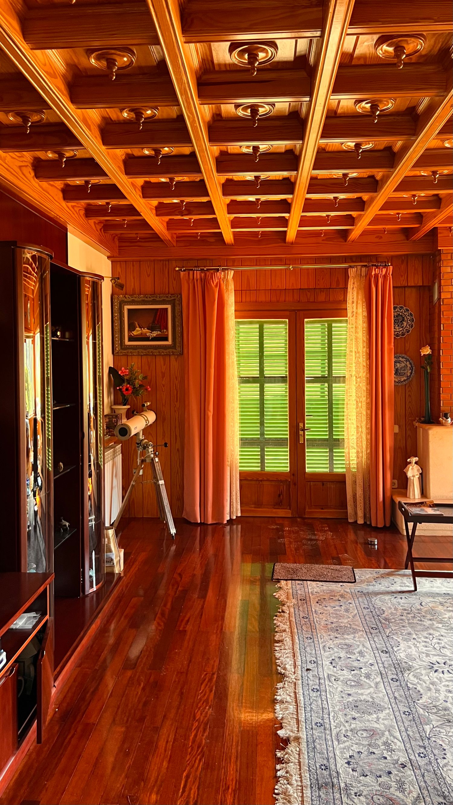 Hallway with wooden coffered ceiling, hardwood floors, and orange curtains framing a green window.
