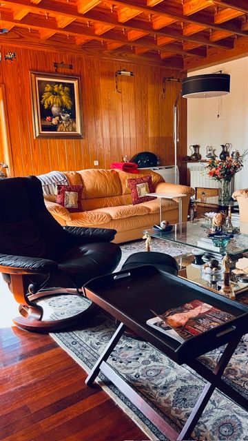 Retro-style living room with wooden ceiling beams, leather furniture, and floral artwork.