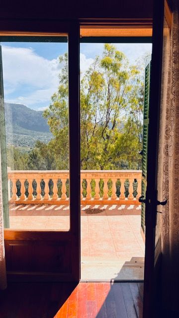 Mountain vista through French doors leading to a terracotta balcony with ornate railings.