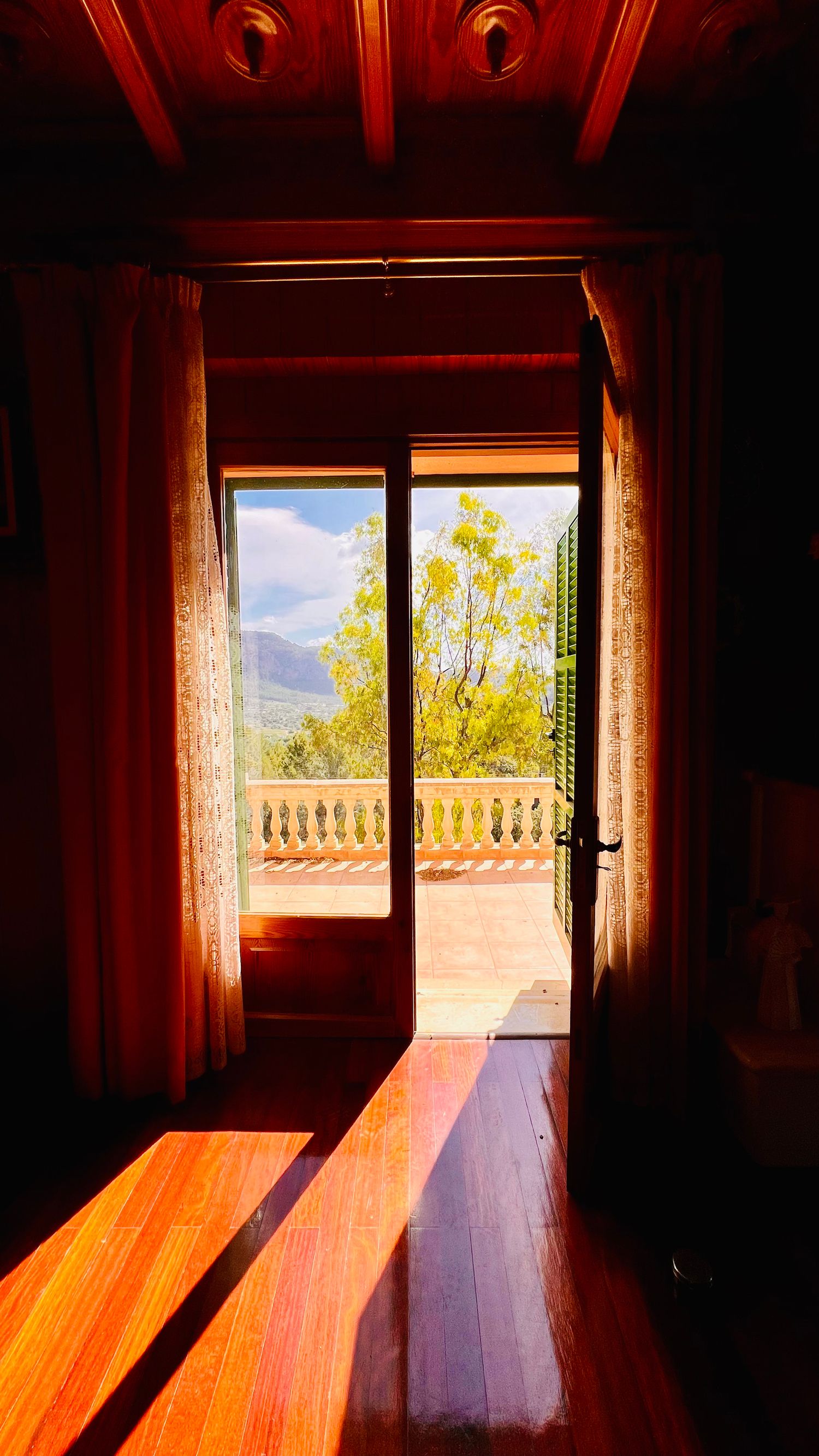 Dramatic doorway framing mountain view through balcony, with sunlight streaming across wooden floors.