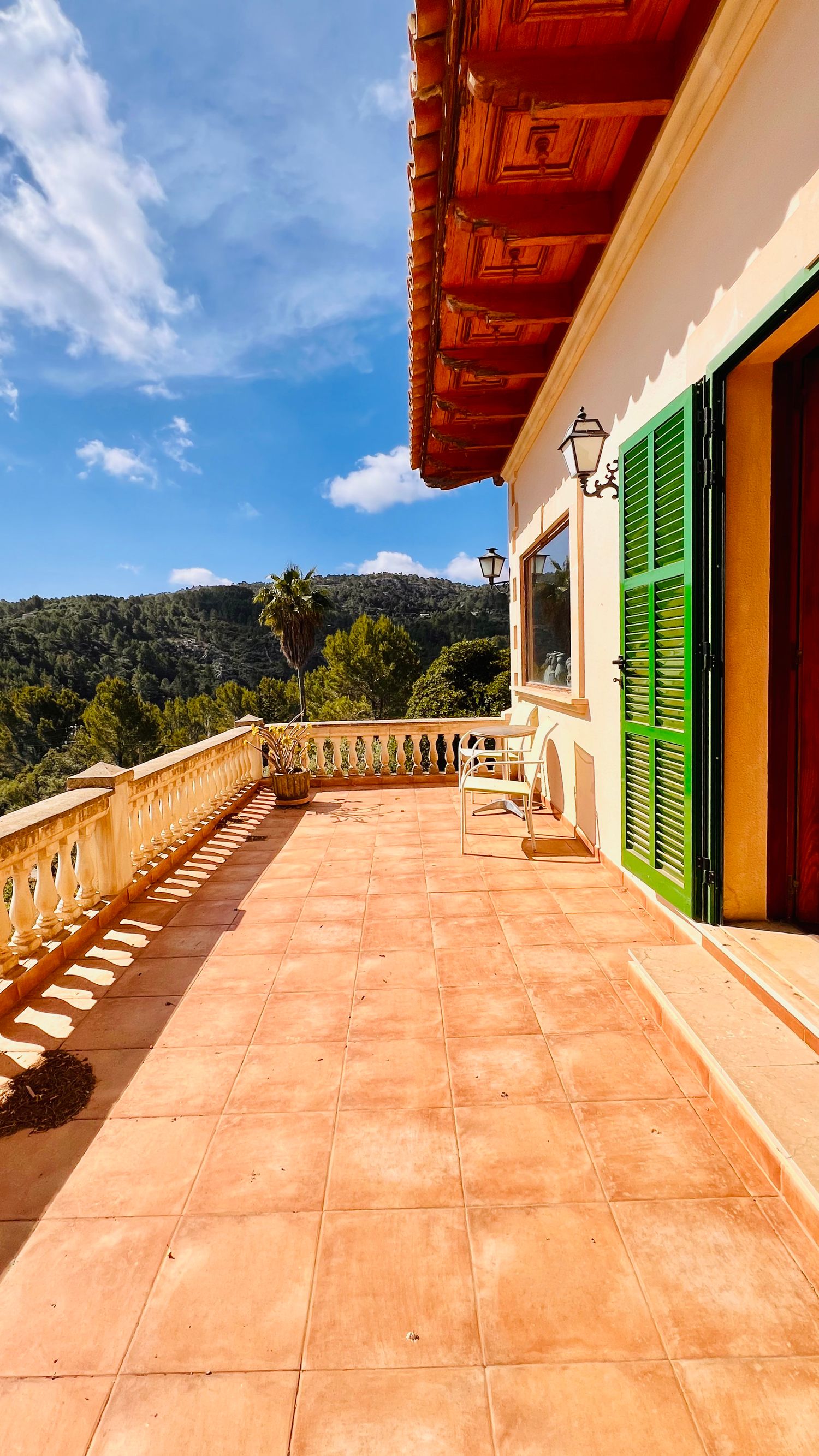 Mediterranean-style terrace with green shutters and mountain views features terracotta tiles and ornate balustrade.