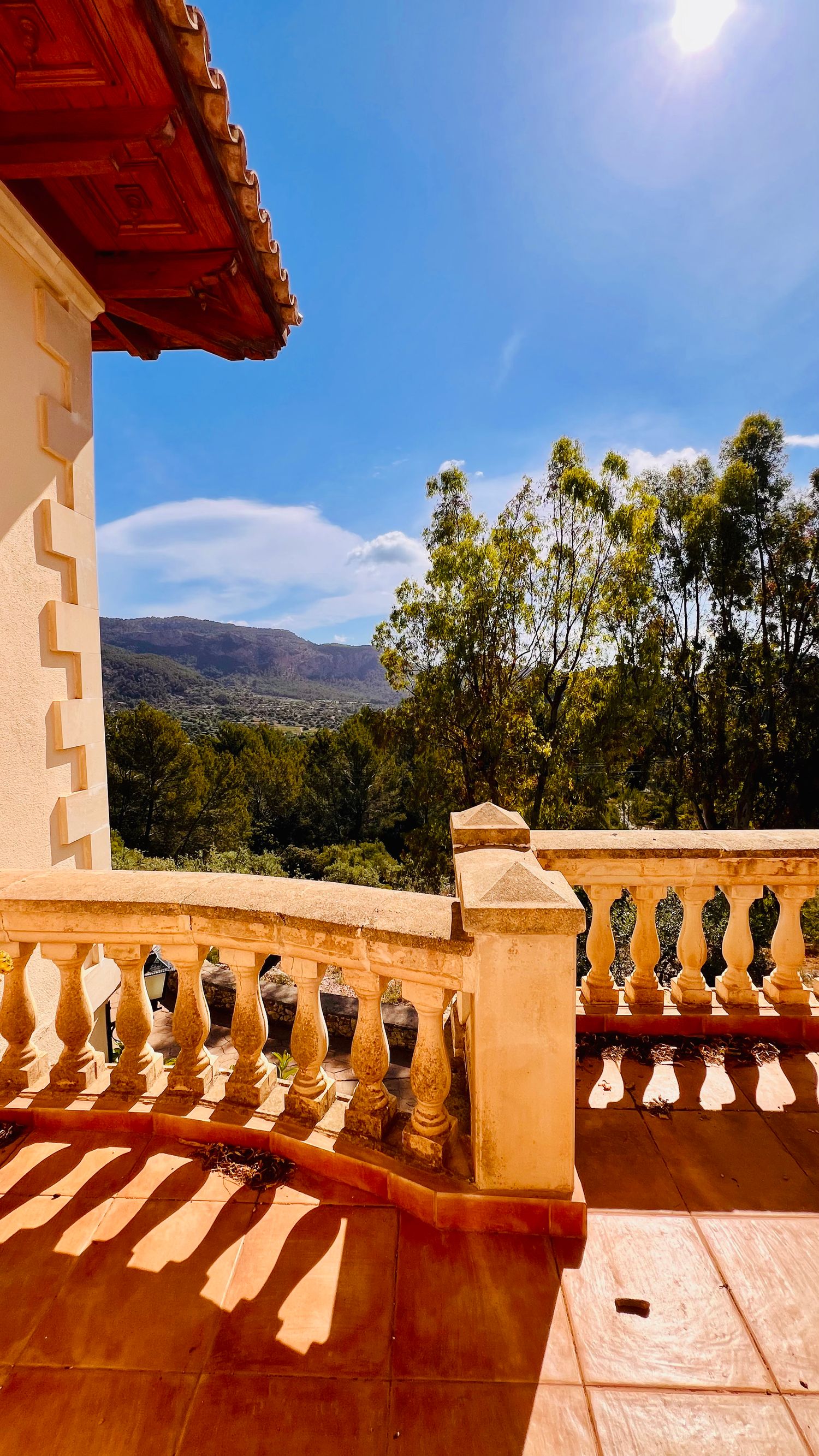 Mediterranean-style balcony with ornate stone railing casting shadows against bright blue sky.
