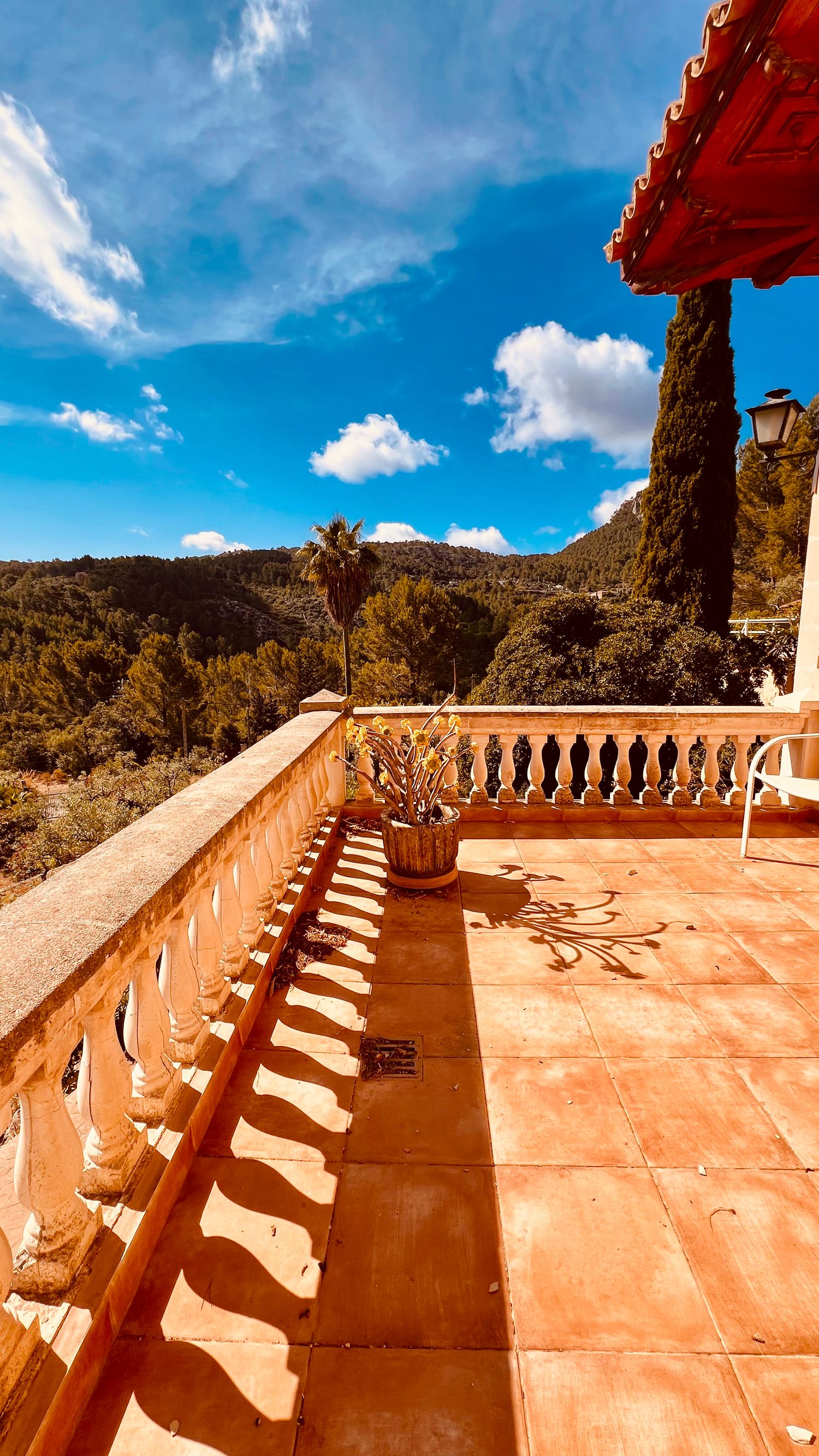 Sun-drenched terrace with terracotta tiles and decorative balustrade overlooking mountain landscape.