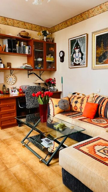 Cozy living room corner with wooden furniture, floating shelves, patterned cushions, and decorative wall art.